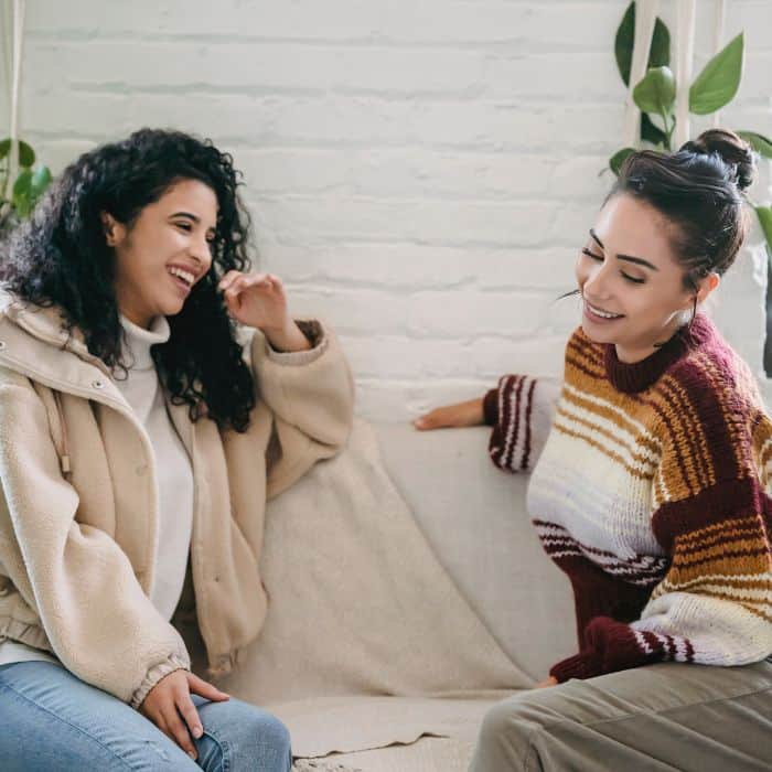 Two women wearing winter sweaters are sitting next to each other on the couch.