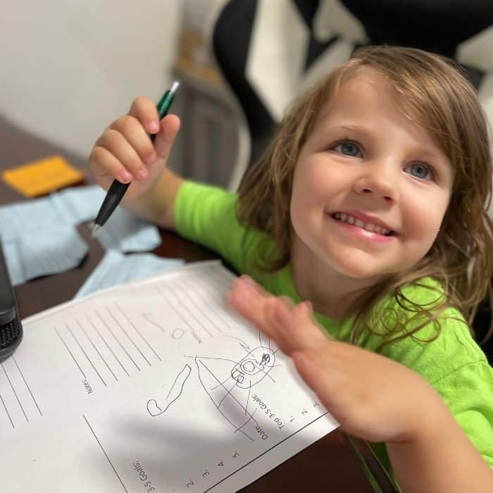 A preschooler is writing down goals and coloring on a worksheet curriculum.