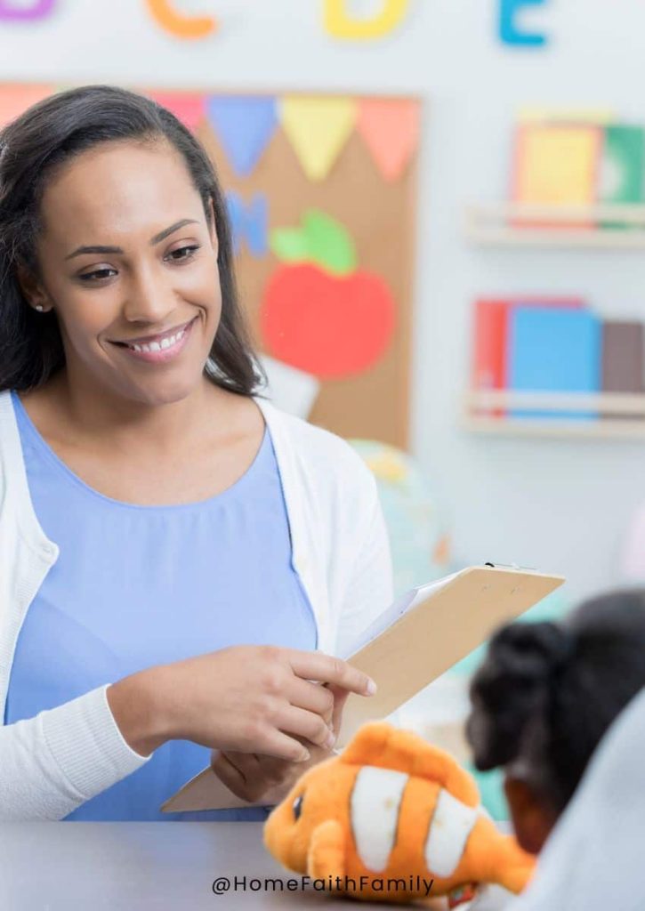 A preschool teacher standing at the front of the classroom with a student.